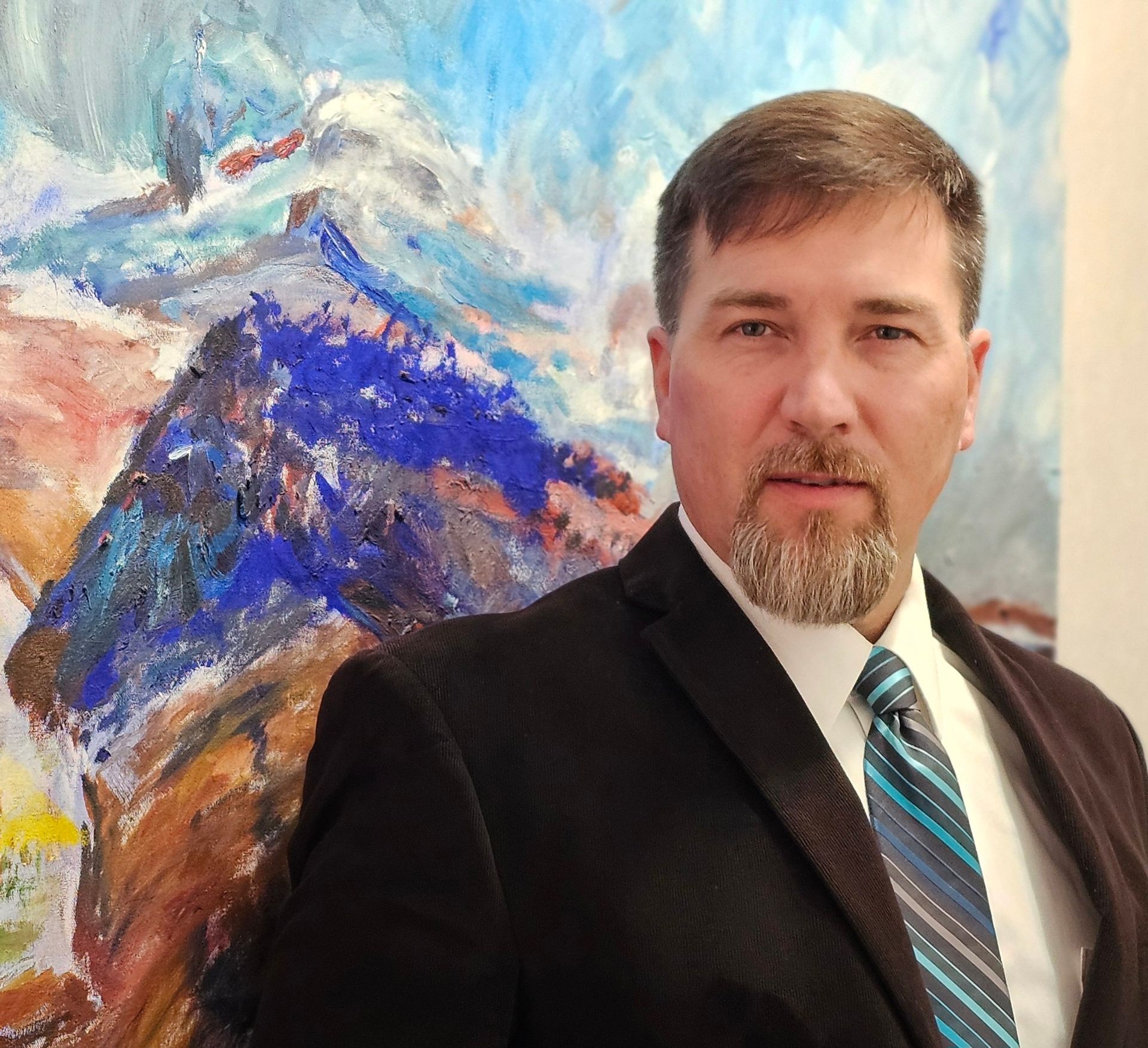 Man in a suit and tie standing in front of a colorful abstract painting.